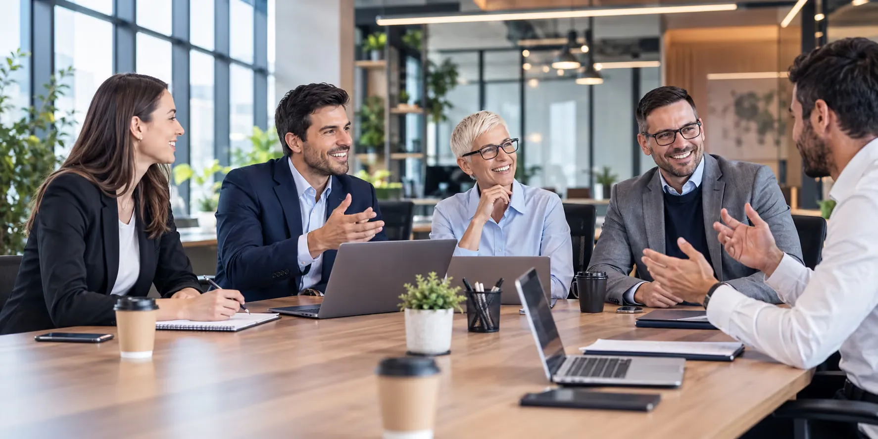 Five people around a meeting table with laptops, smiling